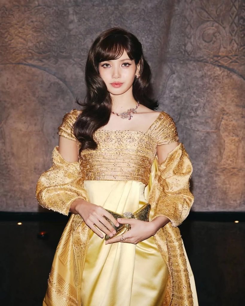 作為年度觀光大使，Lisa 以一襲復刻自泰國國母詩麗吉王后的訂製禮服參加「Amazing Thailand Exclusive Night」活動。那件向 1960 年代 Pierre Balmain「Nuit à Londres」系列致敬的華服，絲質面料在佛塔金光映襯下流動著，泰式傳統剪裁遇上法式高訂工藝，絲綢在佛塔燈光下泛著柔和光澤，每個角度都美得像幅油畫。Bvlgari「La Dolce Vita」項鍊,鑽石在湄南河夜風中閃爍，配上背景的寺廟輪廓，整個氛圍夢幻到不行。